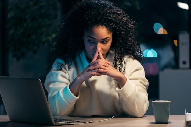 Schot van geconcentreerde Afrikaanse zakenvrouw die denkt tijdens het werken met een laptop op kantoor thuis.