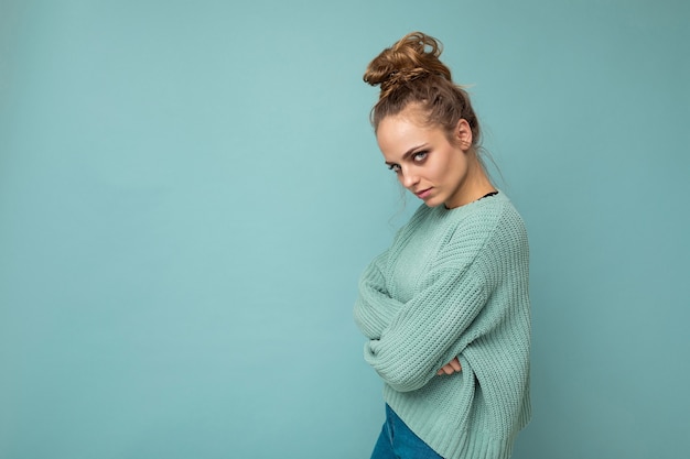 Schot van jonge triest boos ontevreden boze mooie blonde vrouw gekleed in blauwe trui geïsoleerd op blauw