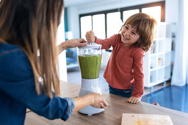 Schot van jongen die zijn moeder helpt bij het bereiden van een detox-sap met blender in de keuken thuis.