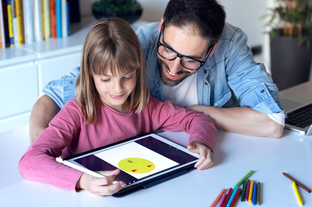 Schot van knappe jonge vader met zijn dochter tekenen met digitale tablet thuis.