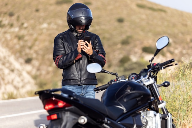 Schot van man motorrijder die aan de telefoon praat met de verzekering van zijn motorfiets na een pech onderweg te hebben gehad.