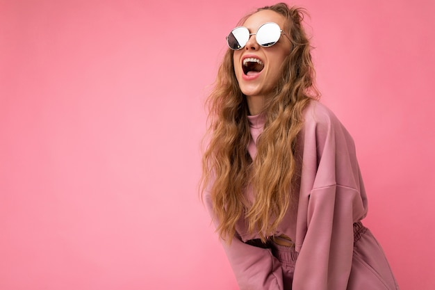 Schot van mooie gelukkige jonge donkerblonde krullende vrouw geïsoleerd over roze muur als achtergrond