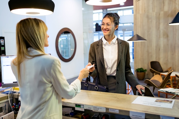 Schot van mooie zakenvrouw neemt kamersleutelkaart en check-in bij de receptie van het hotel.