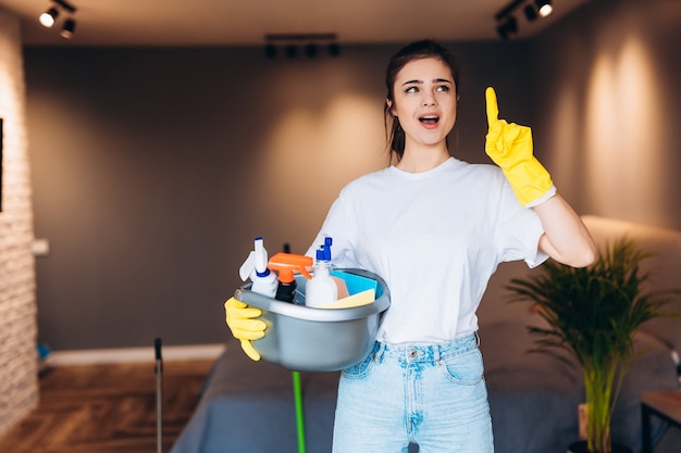 Schot van verrast schoonmaak huishoudster in gele handschoen met wasmiddelen in de woonkamer