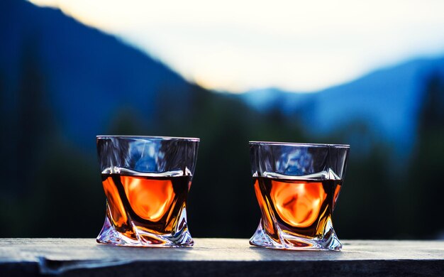 Schot van whisky bij dramatische zonsonderganghemel op de achtergrond van het berglandschap