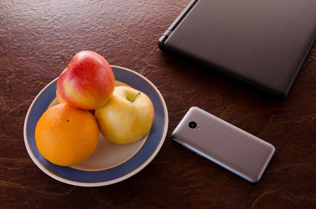 Foto schotel met fruit, een smartphone, een laptop op tafel, bovenaanzicht