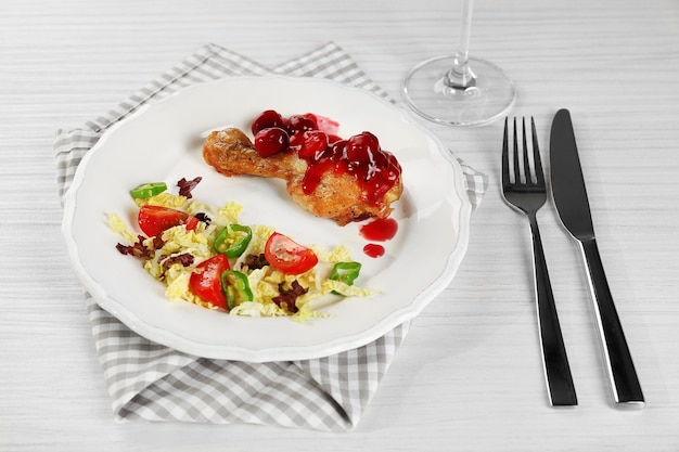 Schotel met gebakken kippenbeen en groentensalade op een wit bord met een glas wijn op tafel met een servet close-up