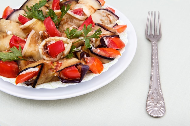 Schotel van gebakken aubergineplakken met tomaten en kaassaus versierd met peterseliebladeren op witte plaat