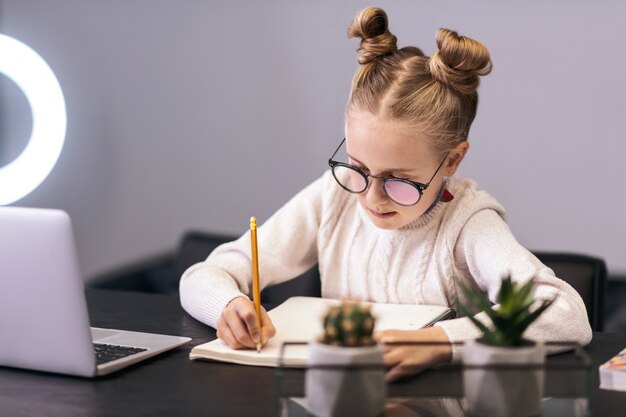 Schrijven. leuk blauwogig langharig meisje dat een witte sweater draagt die iets in een notitieboekje schrijft