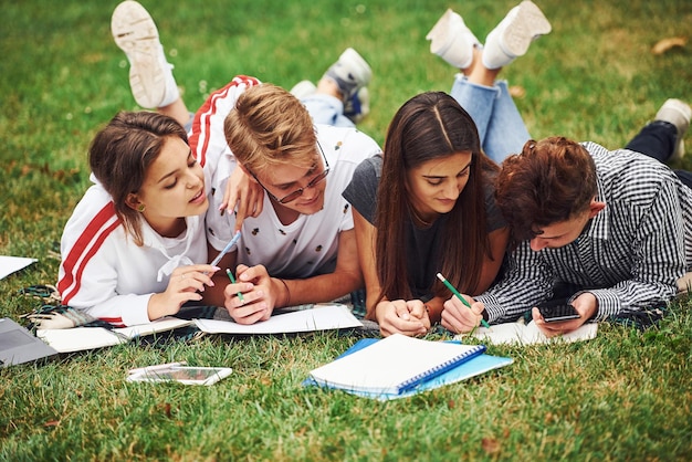 Schrijven op papier. vooraanzicht. Groep jonge studenten in vrijetijdskleding op groen gras overdag.