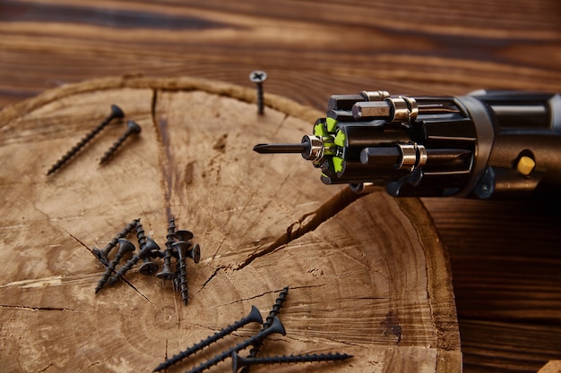 Schroevendraaier en zelftappende schroeven op boomstronk, close-up, houten tafel. Professioneel instrument, timmermansuitrusting, houtbewerkingsgereedschap