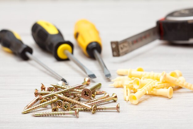 Schroevendraaiers, meetlint en schroeven met plastic pluggen op witte houten ondergrond