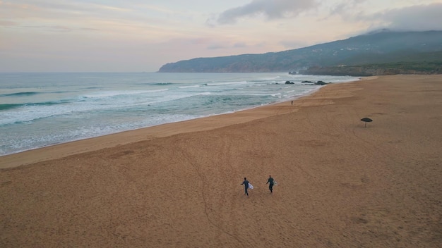 Schuimende zeegolven rollen op het zandstrand drone view surfers lopen langs de kust