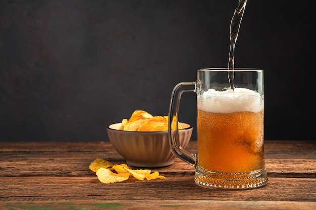 Schuimig bier gieten in een mok op een houten tafel met chips