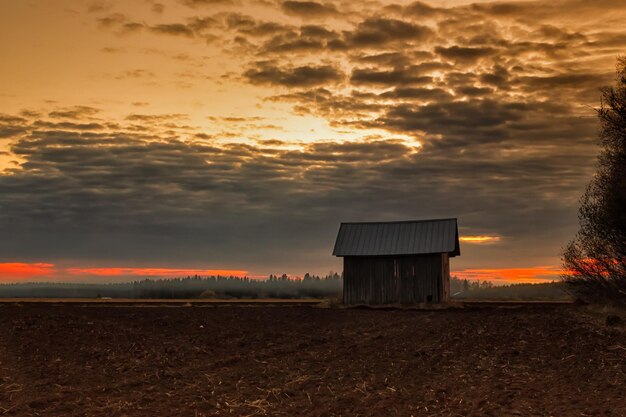 Schuur op het veld tegen bewolkte lucht bij zonsondergang