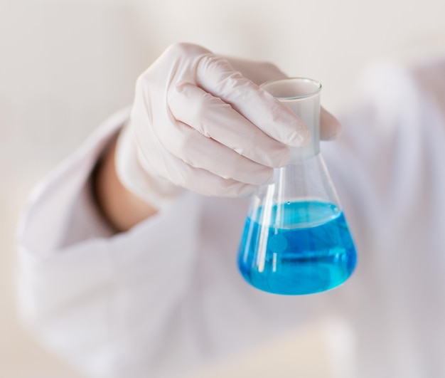 science, chemistry, biology, medicine and people concept - close up of female scientist with flask making test or research in clinical laboratory