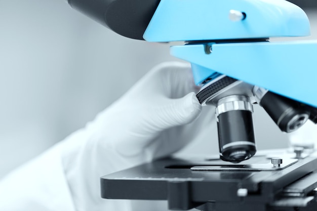 science, chemistry, biology, medicine and people concept - close up of scientist hand in glove setting microscope and making research in clinical laboratory