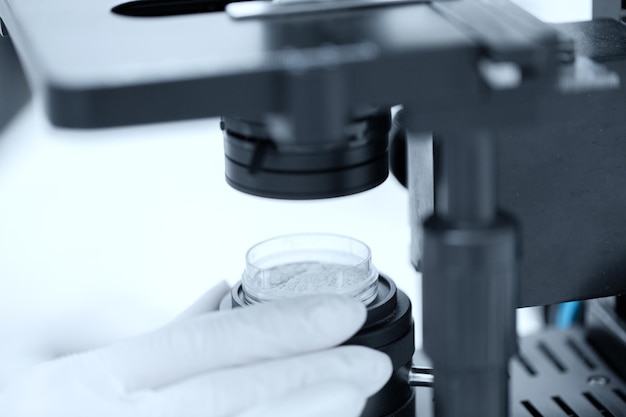 science, chemistry, biology, medicine and people concept - close up of scientist hands with microscope and powder test sample making research in clinical laboratory