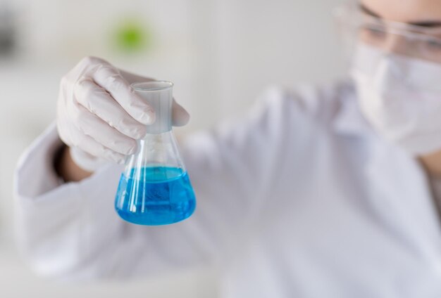 science, chemistry, biology, medicine and people concept - close up of young female scientist with flask making test or research in clinical laboratory