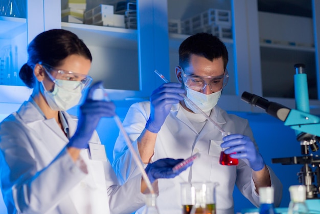 과학, 화학, 생물학, 의학 및 사람 개념 - 임상 실험실에서 테스트 또는 연구를 하는 피펫과 플라스크를 가진 젊은 과학자들