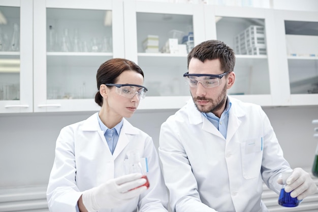 science, chemistry, biology, pharmacy and people concept - young scientists with pipette and flask making test or research in clinical laboratory