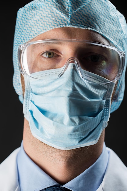 science, chemistry, medical equipment and people concept - close up of scientist face in goggles, protective mask and hat over black background