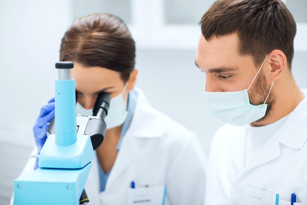 наука, химия, технология, биология и концепция людей - молодые ученые в масках смотрят в микроскоп и проводят тесты или исследования в клинической лаборатории