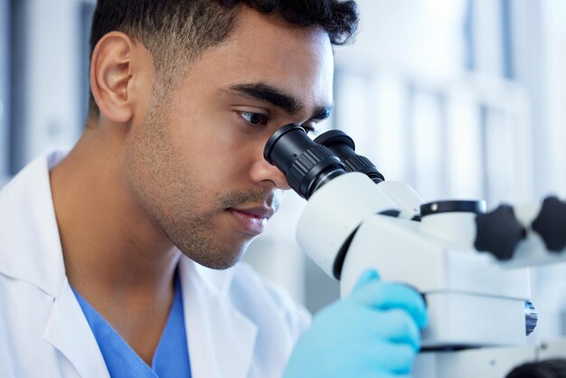 Foto innovazione scientifica e un uomo con microscopio in un laboratorio per la ricerca e l'analisi medica medicina seria e uno scienziato che controlla la chimica microbiologia o un virus che lavora in una clinica