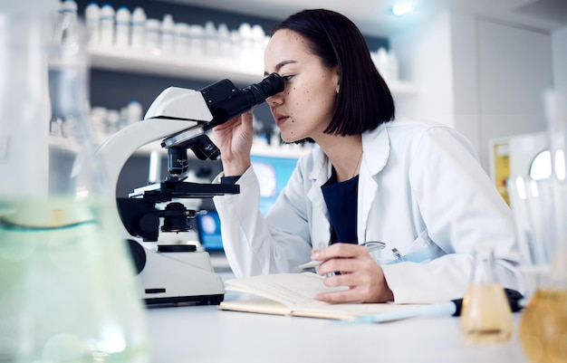 Science microscope and writing with a doctor woman doing research in her laboratory for innovation Healthcare zoom and notebook with a female scientist working in a lab for medical development