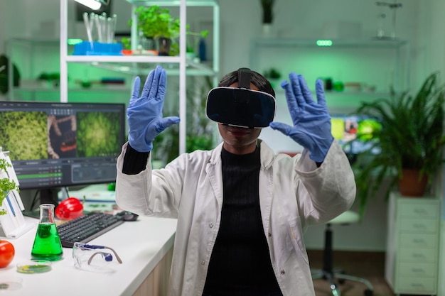 Biologo scienziato che conduce ricerche utilizzando la realtà virtuale facendo il gesto della mano per l'agronomia guardando il campione