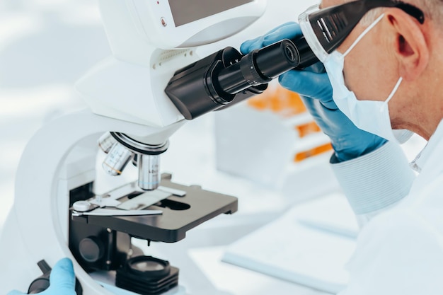 Scientist biologist in a protective mask looking through a microscope