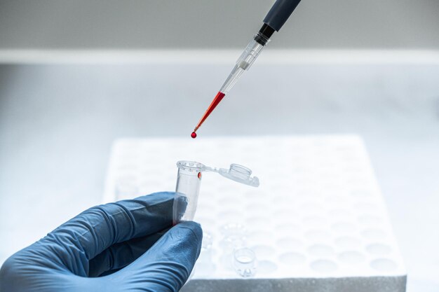 A scientist in blue gloves gently squeezes a red liquid from a pipette into a container