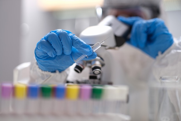 Scientist chemist in protective suit looking through microscope in laboratory closeup