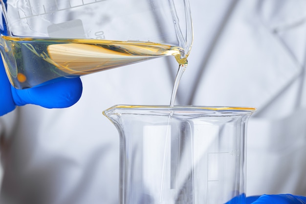 Scientist or doctor in blue gloves pouring some yellow liquid into a flask