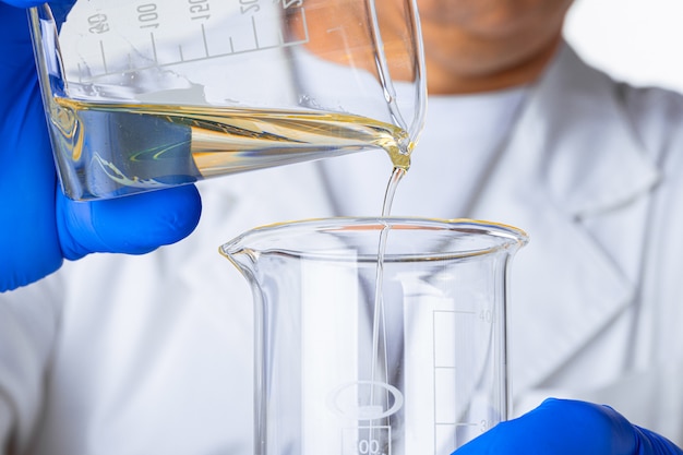 Photo scientist or doctor in blue gloves pouring some yellow liquid into a flask