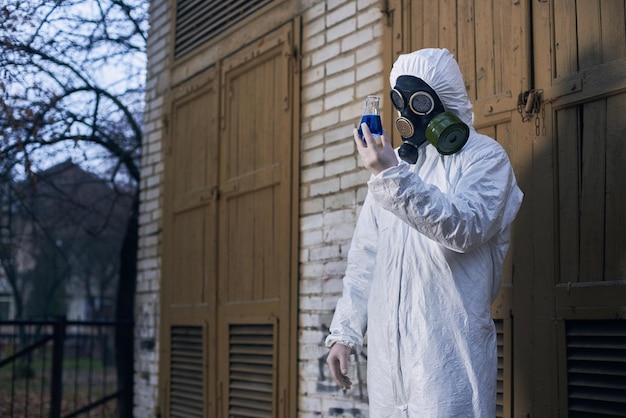 白いつなぎ服と防毒マスクを身に着けて屋外で研究をしている科学者