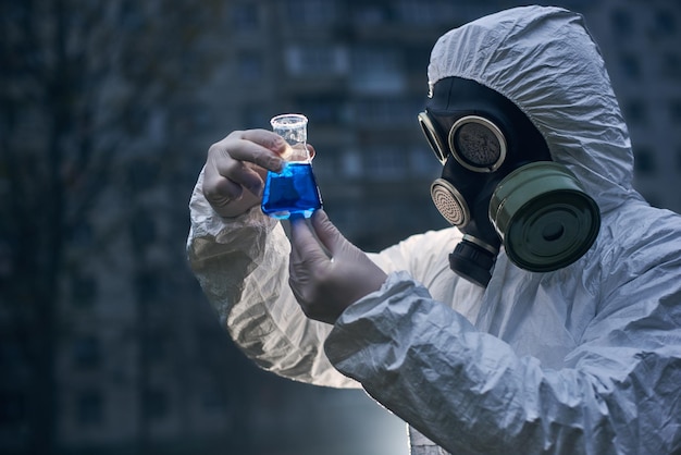 Scientist doing research outdoors wearing white coverall and gas mask