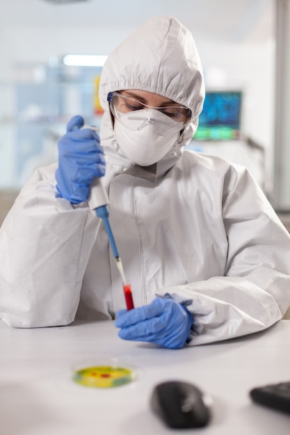 Scientist dressed in ppe suit taking blood sample using micropipette