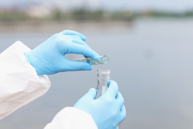 Scientist in gloves and protective suit pours dirty water from test tube into flask water