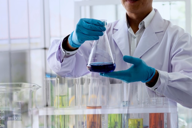 Scientist is looking at Erlenmeyer flask to observe the chemical reaction in chemical laboratory.