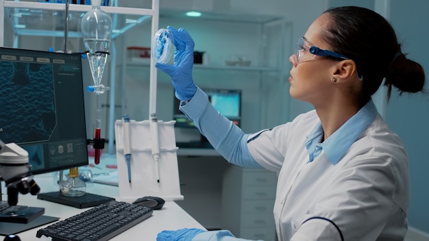 Scientist in laboratory analyzing petri dish with liquid bacteria