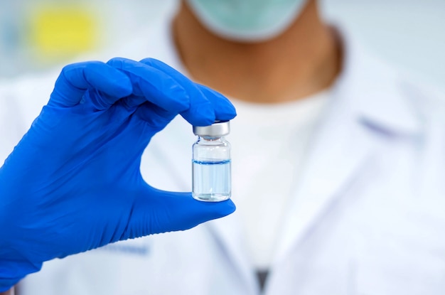 Ученый в лаборатории держит бутылку с жидкими вакцинами