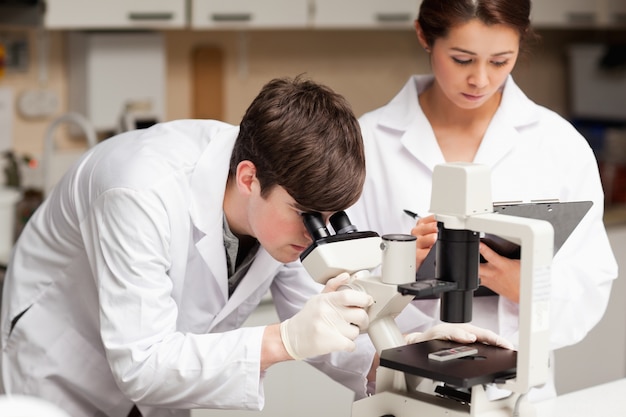 Scientist looking in a microscope while his colleague is taking 