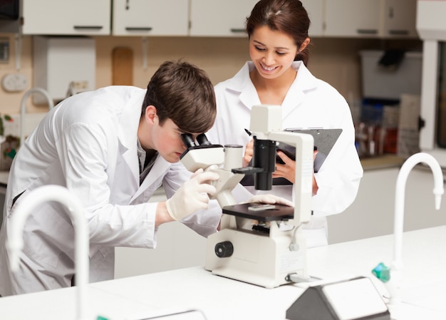 Scientist looking in a microscope while his coworker is taking n