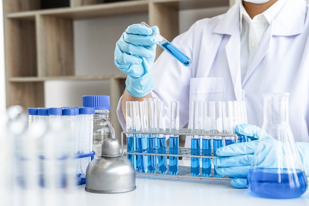 Scientist or medical in lab coat holding dropper with reagent, mixing reagents in glass flask