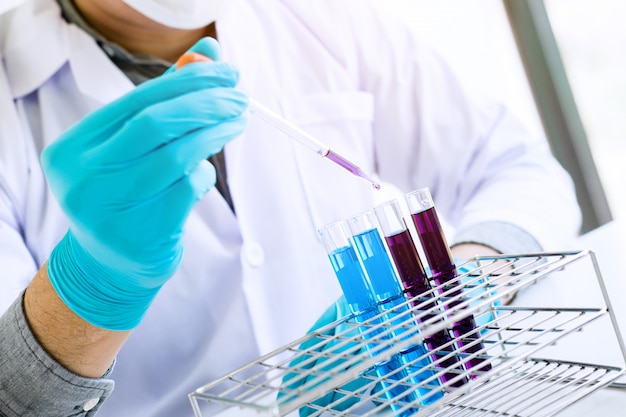 Foto scienziato o medico in camice da laboratorio che tiene la provetta con il reagente con goccia di liquido di colore