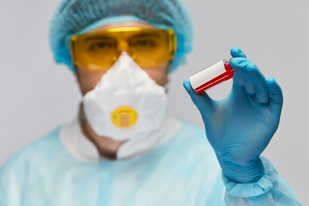 Scientist in medical protective suit holding test tube with white mark and red liquid