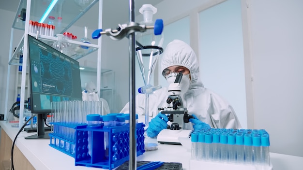 Scientist microbiology lab in protective suit conducting virus analysis looking through microscope. Team of doctors examining virus evolution using high tech for vaccine development against covid19