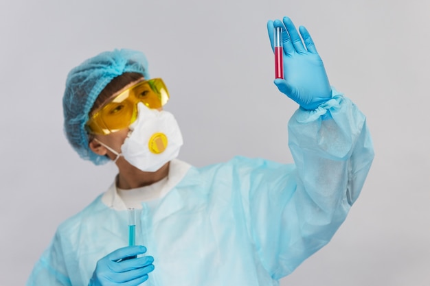 Scientist in protection costume with raspiratory mask holding test tubes with differnt colors of liquid on grey wall