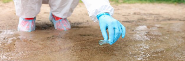 Scientist in protective suit collecting water in test tube from\
lake closeup checking quality